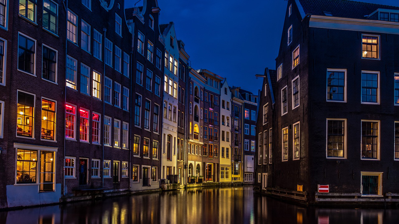 Nighttime view of the Waterbuurt neighborhood in Amsterdam, showcasing a canal lined with illuminated floating homes, demonstrating innovative water-based living solutions.